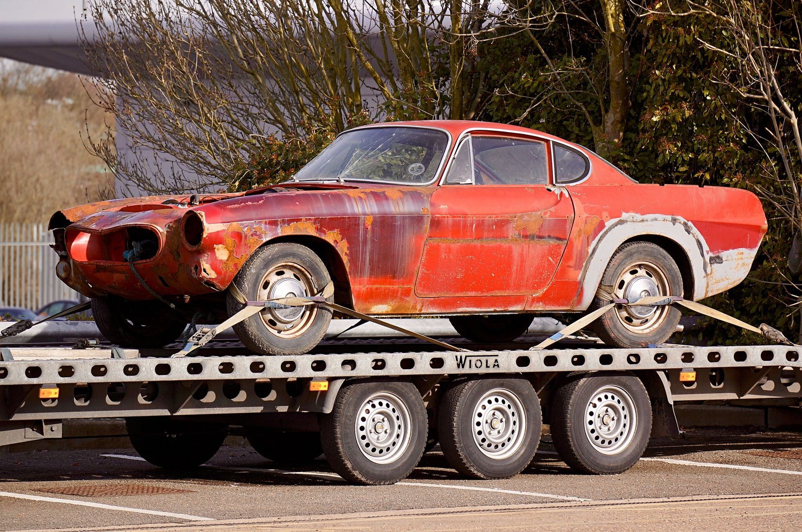 A rusted junk car loaded onto a flatbed tow truck