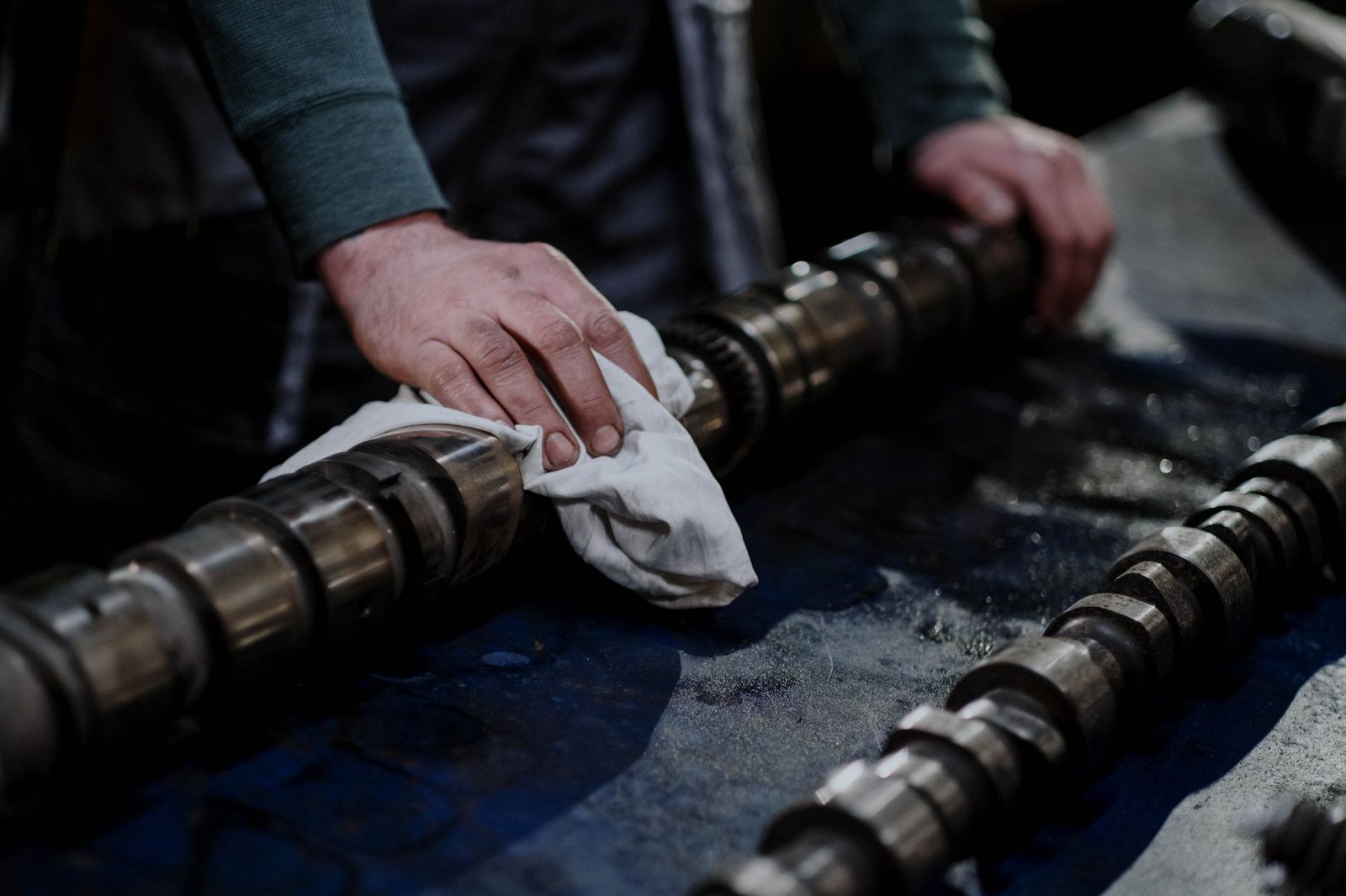 A mechanic cleaning and inspecting a camshaft on a workbench