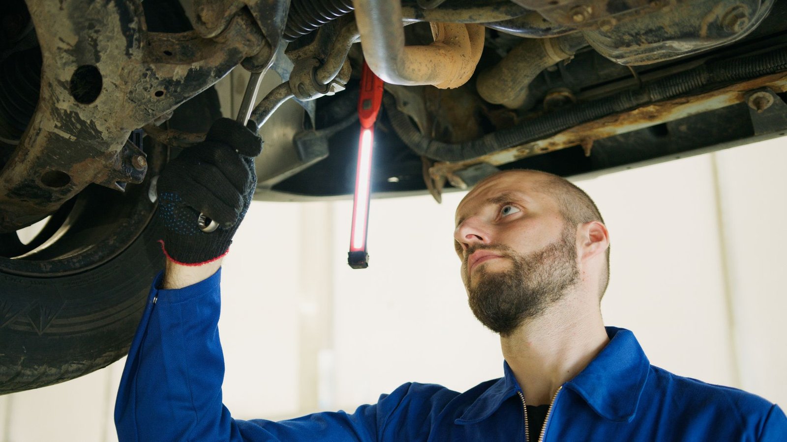 A person working underneath a vehicle with a wrench and work light